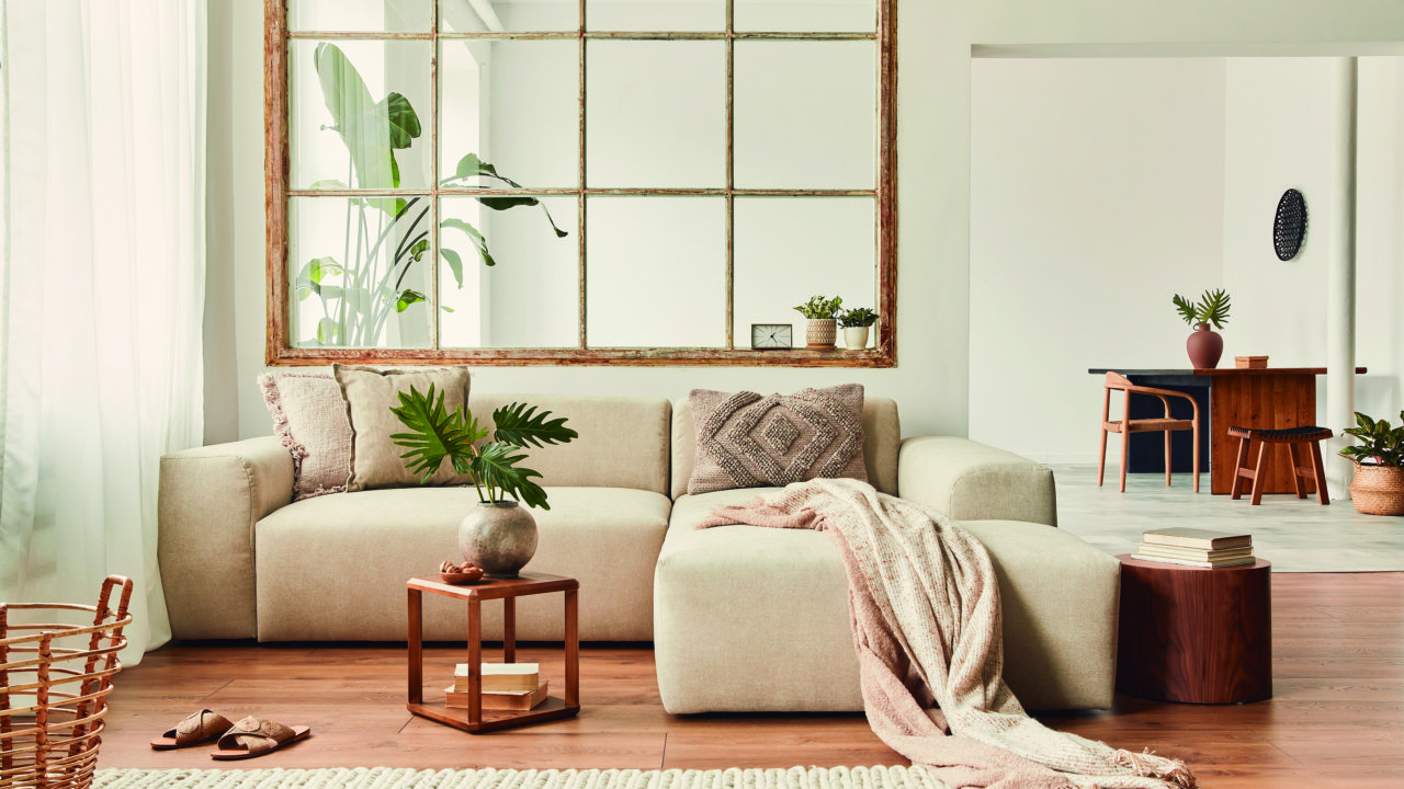 Modern interior of open space with design modular sofa, furniture, wooden coffee tables, plaid, pillows, tropical plants and elegant personal accessories in stylish home decor. Neutral living room.